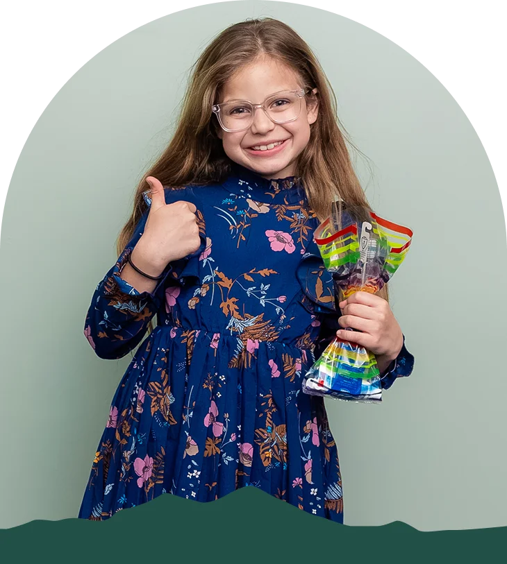 Young patient smiling and giving a thumbs up while holding a goodie bag at Pleasant Valley Pediatric Dentistry