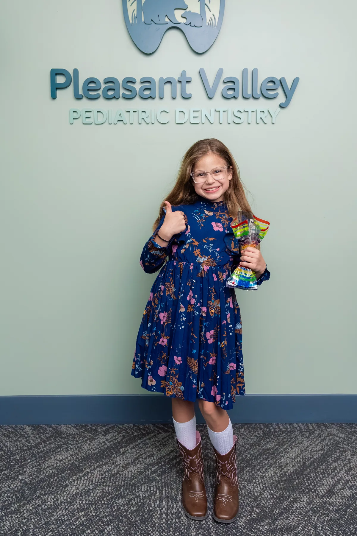 Young girl in a blue dress smiling at Pleasant Valley Pediatric Dentistry